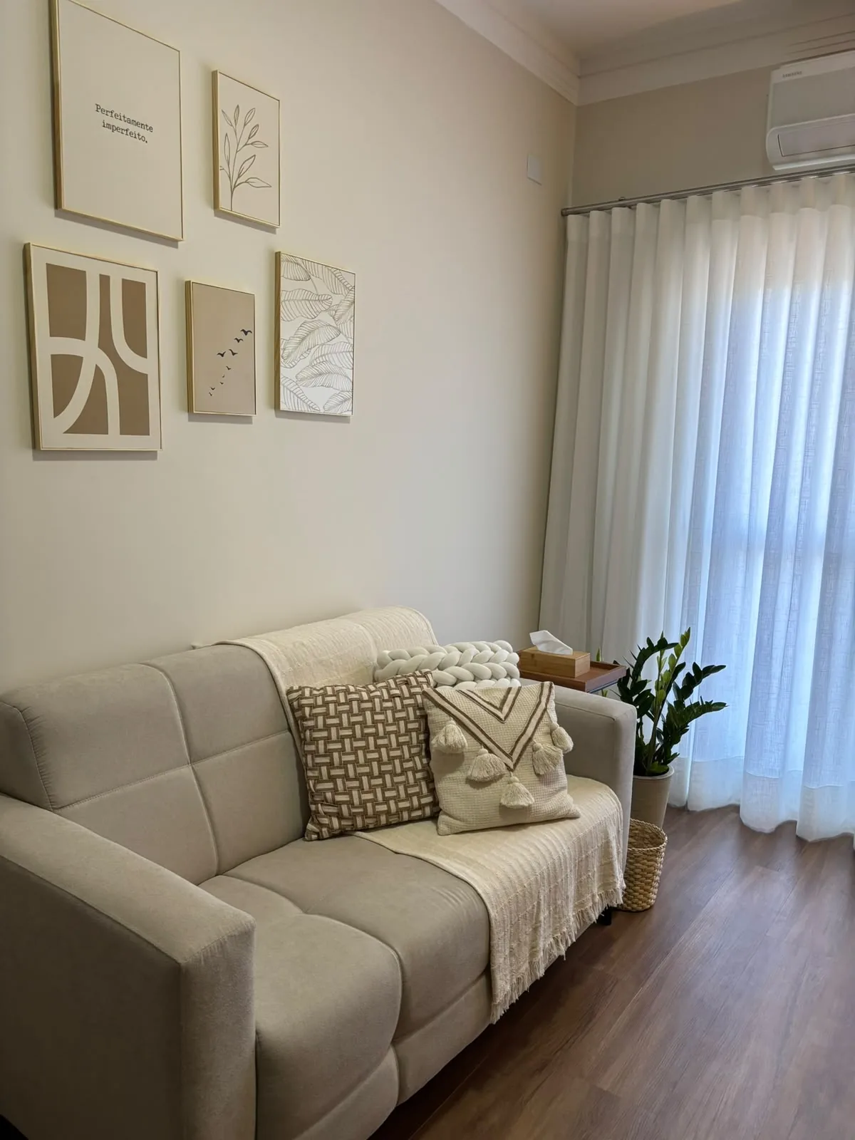 Sala de atendimento aconchegante com sofá bege, almofadas e quadros na parede